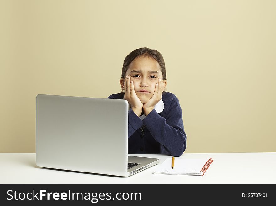 Young girl using laptop on white desk with homework looking bored