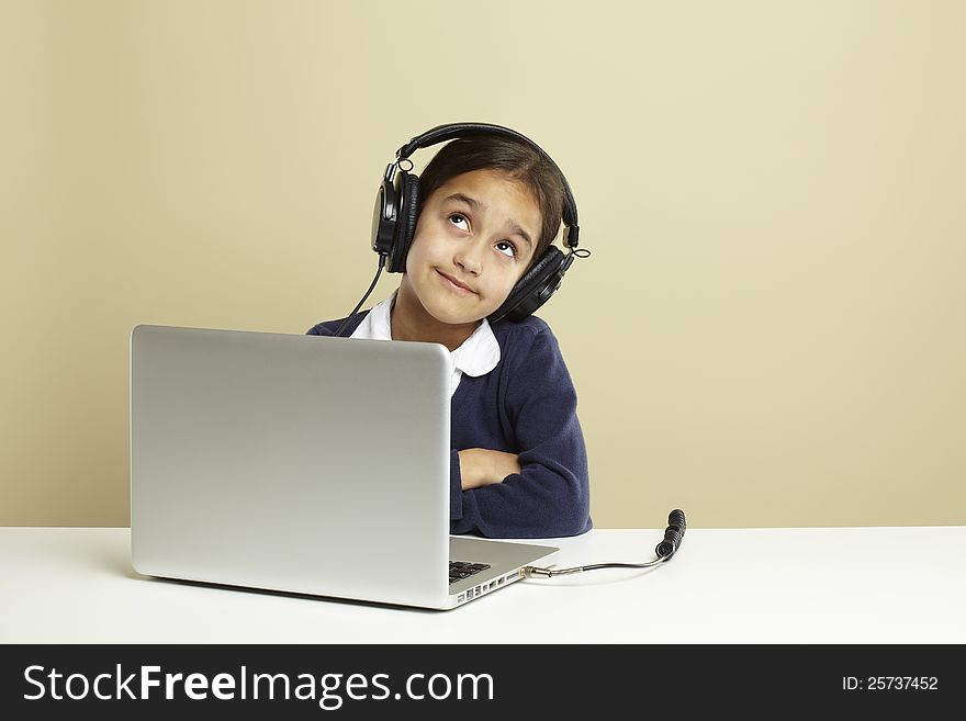 Young girl using laptop on white desk listening to music