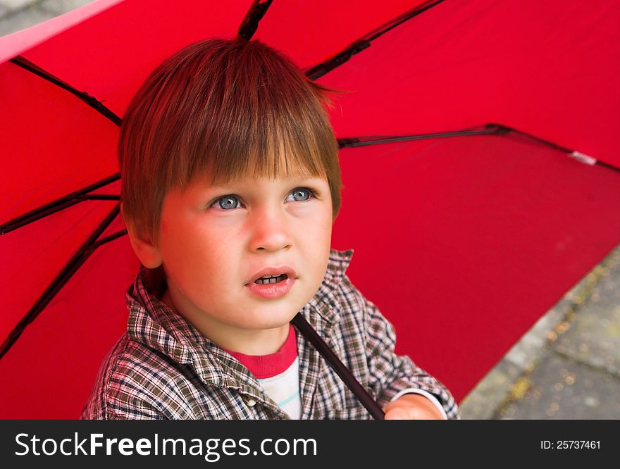 Little boy with a red umbrella in his hand is listening to the rain. His face collected. Little boy with a red umbrella in his hand is listening to the rain. His face collected.