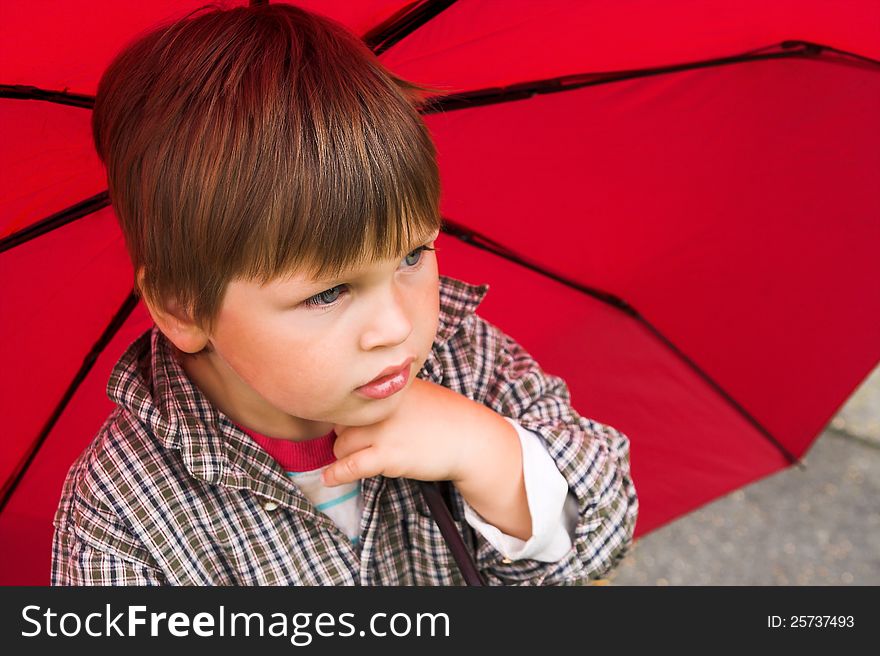 Little boy with a red umbrella in his hand is listening to the rain. His face collected. Little boy with a red umbrella in his hand is listening to the rain. His face collected.