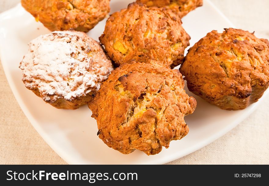 Fresh baked pumpkin muffins on a plate with sugar icing over one of them.