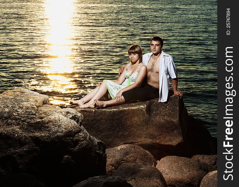 Young couple sitting on rocks near the lake at sunset. Young couple sitting on rocks near the lake at sunset