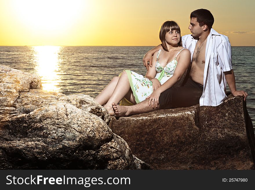 Young couple sitting on rocks near the lake at sunset. Young couple sitting on rocks near the lake at sunset