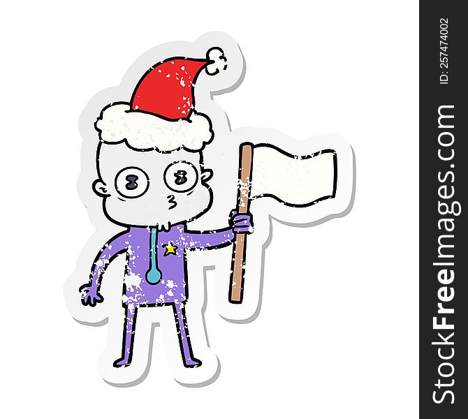 hand drawn distressed sticker cartoon of a weird bald spaceman with flag wearing santa hat