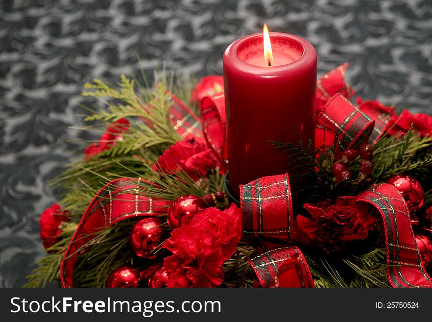 A red candle Christmas decoration set on the right side. It has red carnations and ribbons set in gree boughs. A red candle Christmas decoration set on the right side. It has red carnations and ribbons set in gree boughs