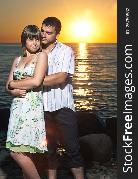 Young couple staying on stones near the lake at sunset. Young couple staying on stones near the lake at sunset