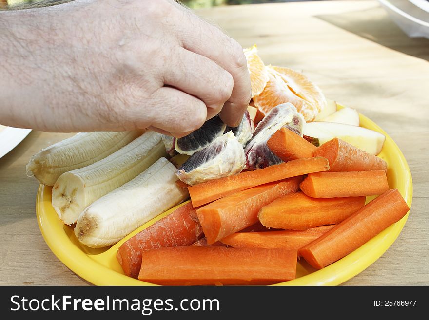 Caucasian male hand taking a wedge of a blood orange from a vegetable and fruit plate outdoors. Caucasian male hand taking a wedge of a blood orange from a vegetable and fruit plate outdoors.