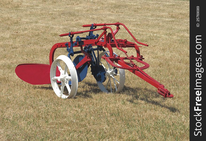 Old tractor pulled two blade American farming plow, sitting in a field. Restored and painted red, white, and blue. Old tractor pulled two blade American farming plow, sitting in a field. Restored and painted red, white, and blue.