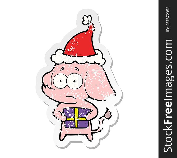 hand drawn distressed sticker cartoon of a unsure elephant with christmas present wearing santa hat