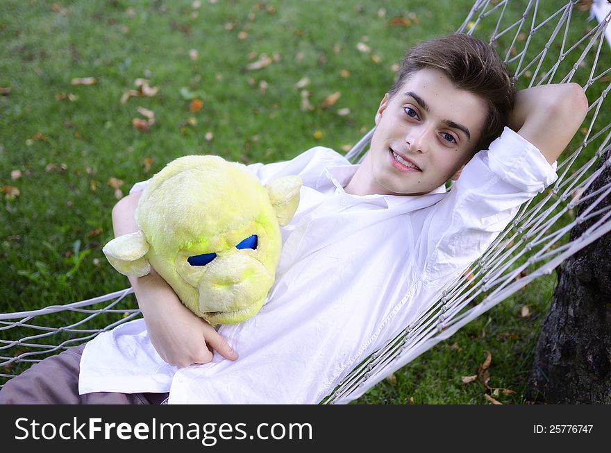 Young man resting in a hammock, holding monkey mask in his hand. Young man resting in a hammock, holding monkey mask in his hand