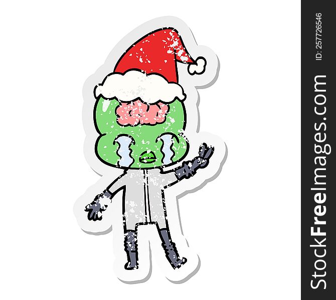 hand drawn distressed sticker cartoon of a big brain alien crying and giving peace sign wearing santa hat