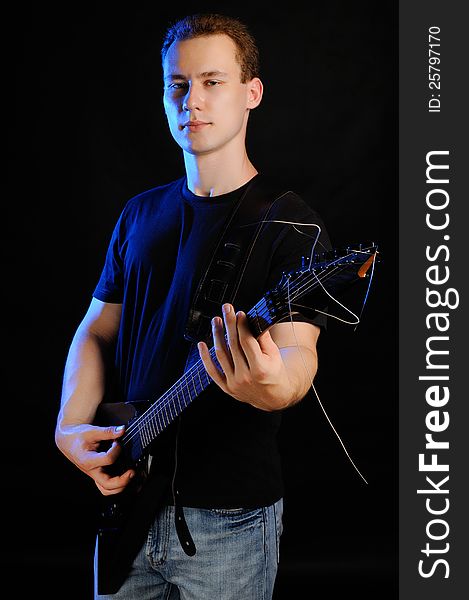 A young guy with an electric guitar on a black background. A young guy with an electric guitar on a black background