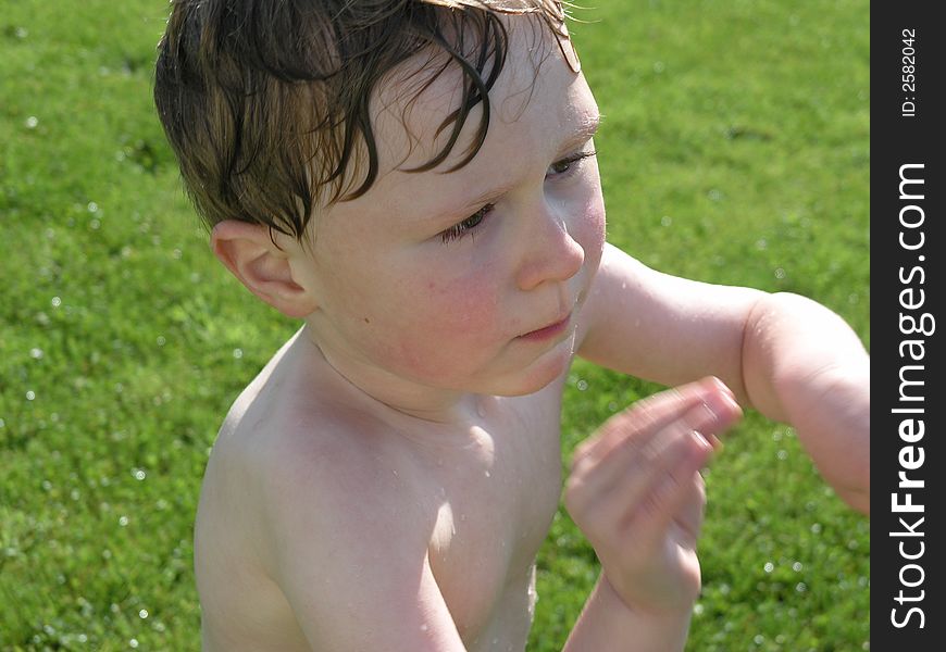 Wet boy playing outside with green grass background. Wet boy playing outside with green grass background