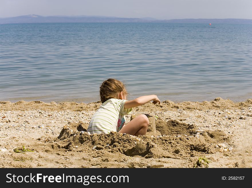 The girl plays on seacoast, sand