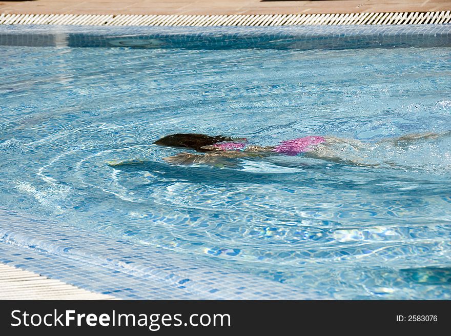 A girl swims underwater in a crystal clear blue pool. A girl swims underwater in a crystal clear blue pool