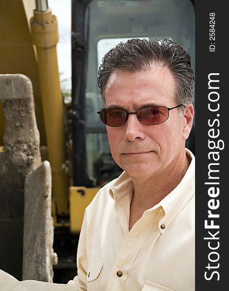 A close up of a supervisor or foreman type standing with a backhoe in the background. A close up of a supervisor or foreman type standing with a backhoe in the background.