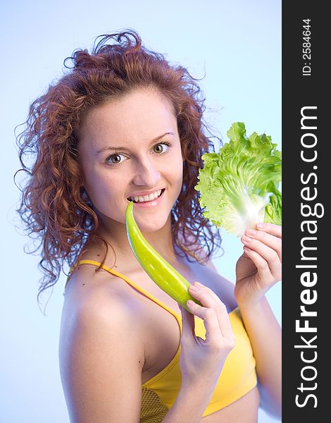 Young happy woman is holding a lettuce leaf and a pepper. Young happy woman is holding a lettuce leaf and a pepper