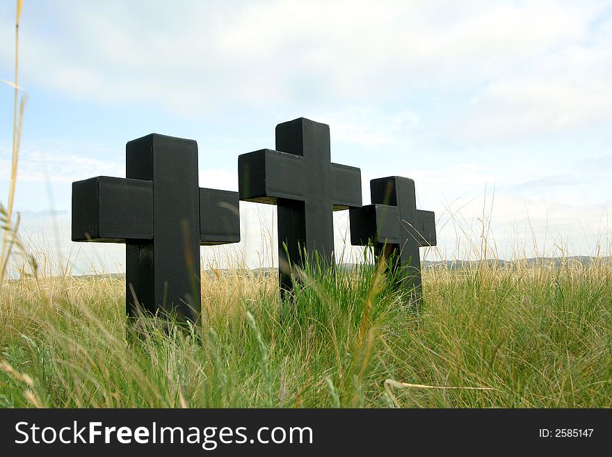 Three black crosses in a grass on a background of the sky