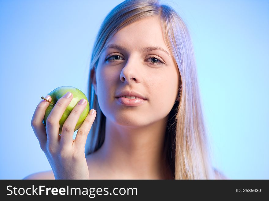 Young blonde woman is holding an apple looking sideways. Young blonde woman is holding an apple looking sideways