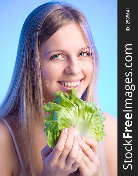 Young blonde woman is holding a fresh lettuce leaf