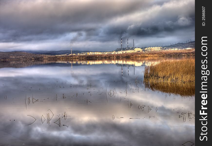 Lake in the north of Russia cloudy day. A factory smoke. Settlement on the bank of lake.