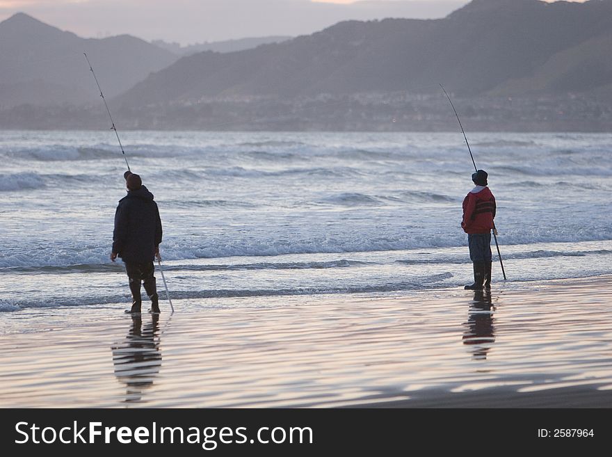 Two men fishing from ocean beach.