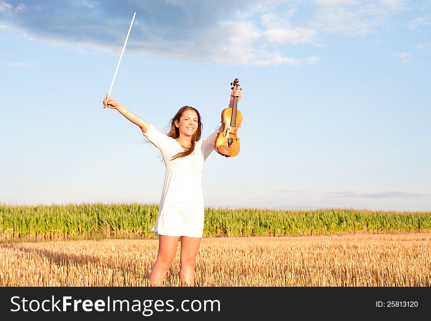 Young woman holding violin and bow outdoors on the field in summer evening