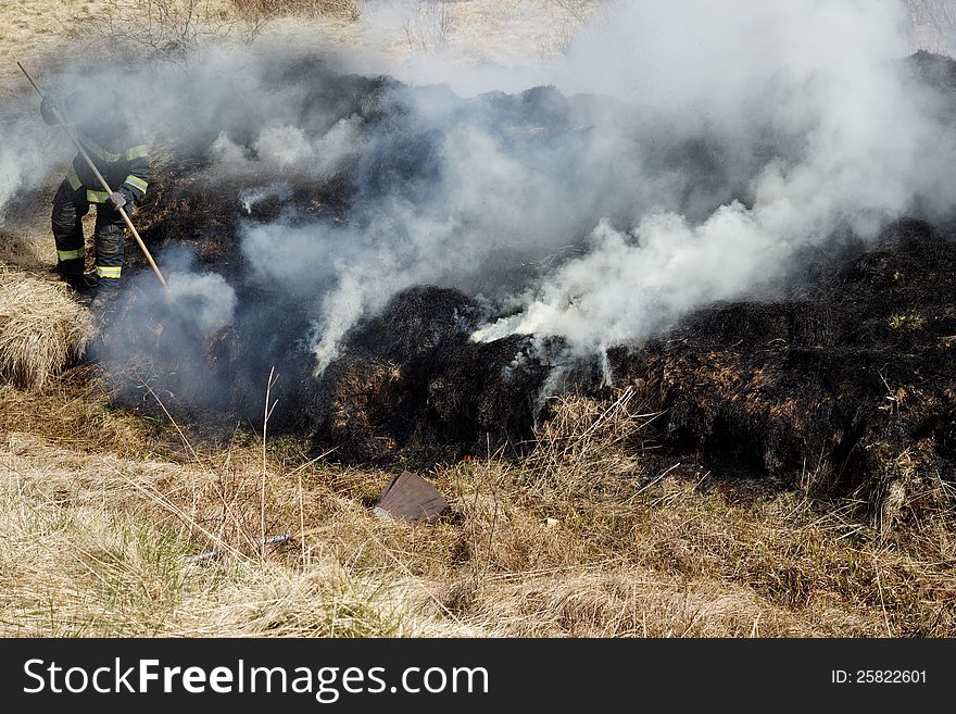 Black and gray grass residues after wildfire. Focus is on the fireman. Black and gray grass residues after wildfire. Focus is on the fireman.