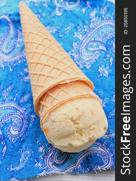 Cone of apricot icecream on blue napkin. Cone of apricot icecream on blue napkin
