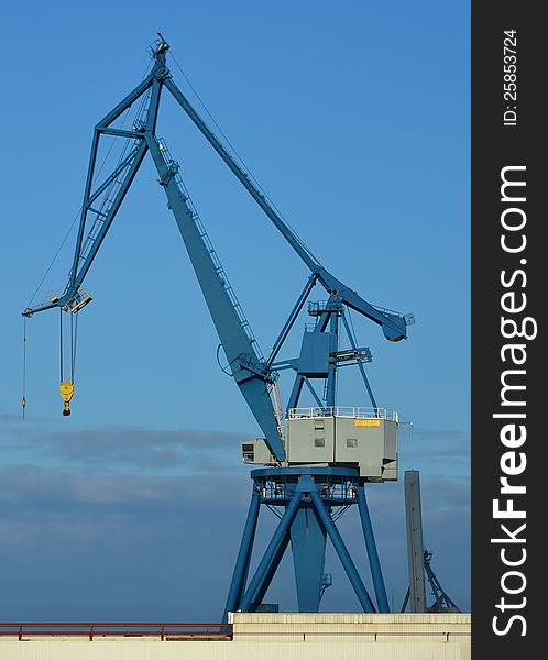 Large blue harbor crane stands idle in the evening sun with yellow hook - resembling a huge insect or spider