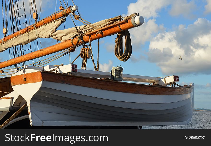 A classic wooden rowboat hangs from the stern of a vintage sail ship. The oiled wood glows orange in the evening sun. A classic wooden rowboat hangs from the stern of a vintage sail ship. The oiled wood glows orange in the evening sun.