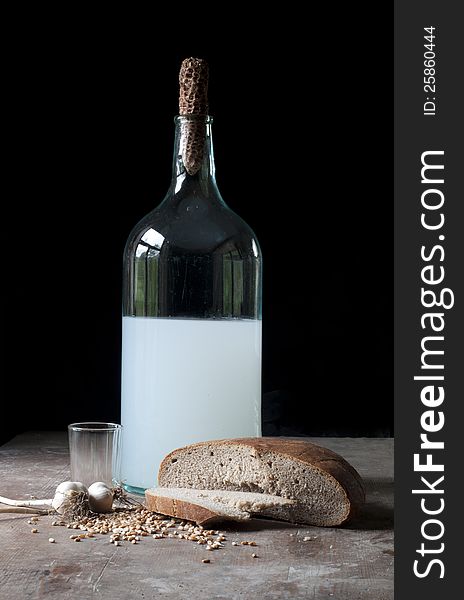 Old bottle with alcohol, wheat, corn, glass and garlic in a rustic cellar