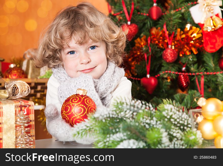 Happy child holding red ball against Christmas tree with decorations. Happy child holding red ball against Christmas tree with decorations