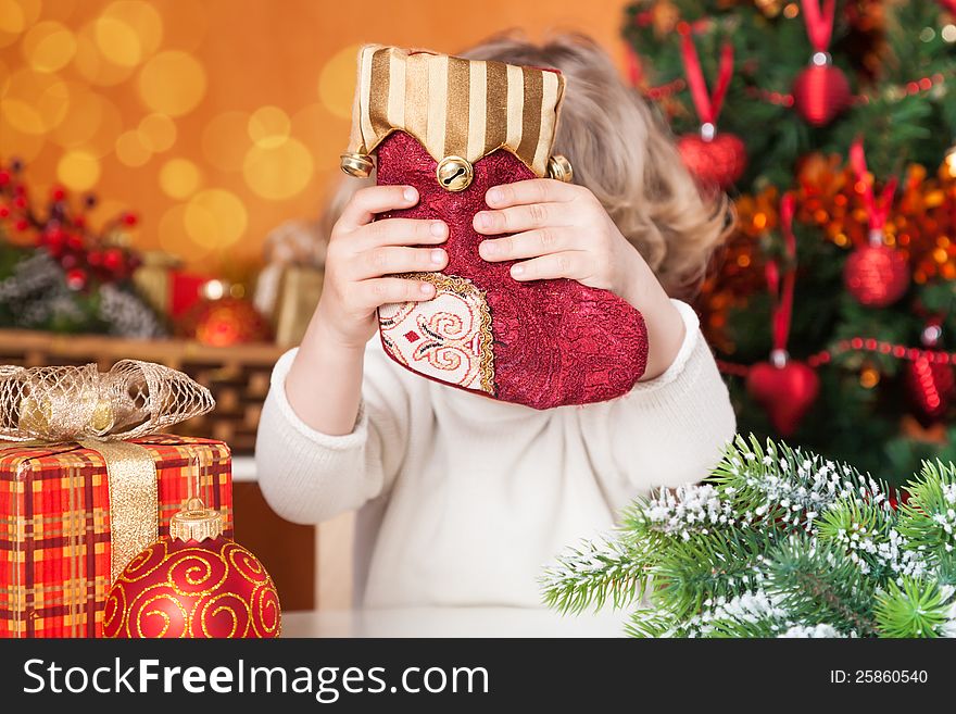 Funny child holding red sock against Christmas decorations background. Funny child holding red sock against Christmas decorations background