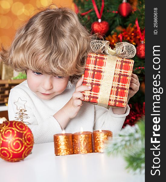 Funny child holding gift against Christmas tree with decorations