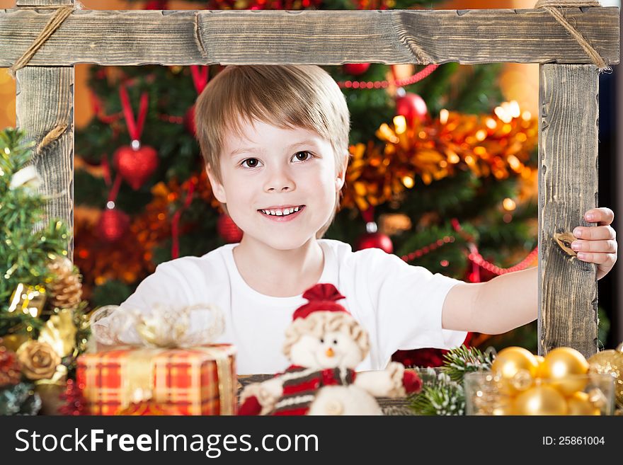 Happy boy looking into wooden frame against decorated Christmas background. Happy boy looking into wooden frame against decorated Christmas background
