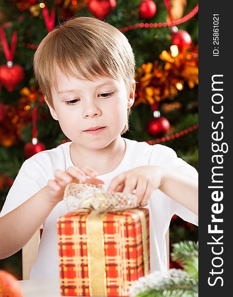 Surprised boy opening present against Christmas tree with decorations. Surprised boy opening present against Christmas tree with decorations