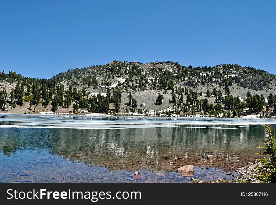 Reflective mountain lake still covered with ice in early spring