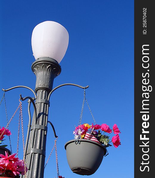 Abstract Concrete Retro Lamp Post against clear blue sky background with flower pots and flowers hanging