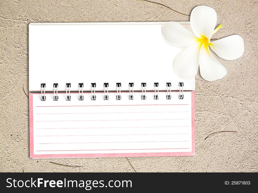 White Notebook With Frangipani Flower On The Sand