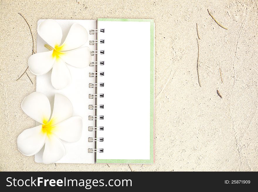 White Notebook With Frangipani Flower On The Sand