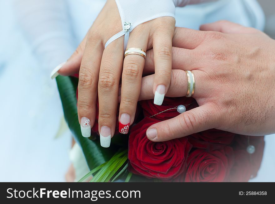 Two hands on bouquet of rose with wedding rings