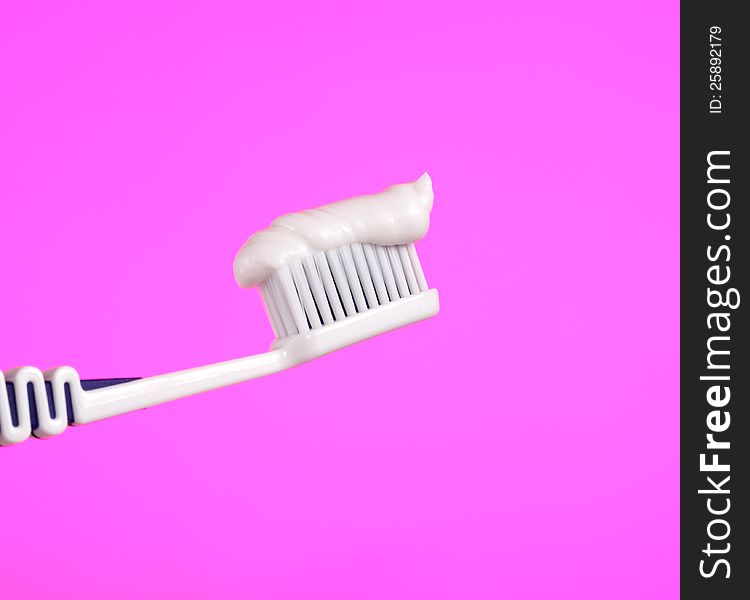 A toothbrush with toothpaste on a bright pink background. A toothbrush with toothpaste on a bright pink background