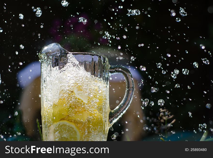 Water pouring and splahing into glass jug filled with lemons on sunny day. Water pouring and splahing into glass jug filled with lemons on sunny day.