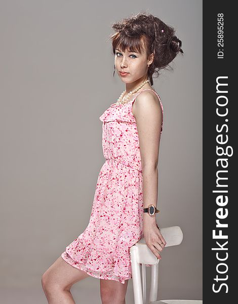 Beautiful girl posing in a pink dress relies on a chair. Beautiful girl posing in a pink dress relies on a chair