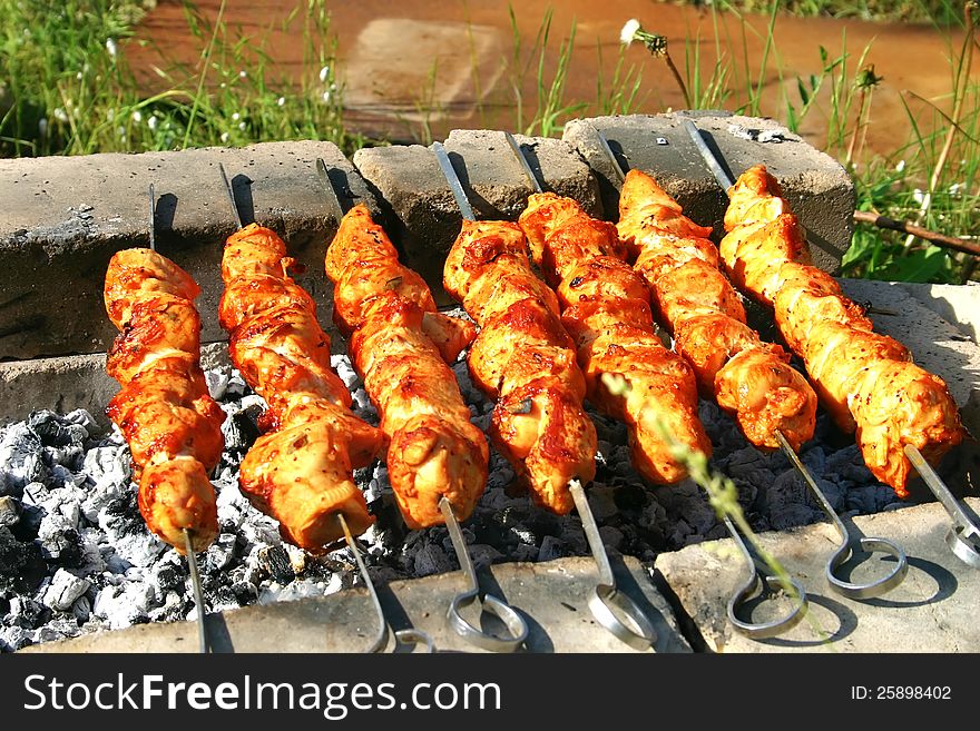 Meat grilled on metallic skewers over a fire
