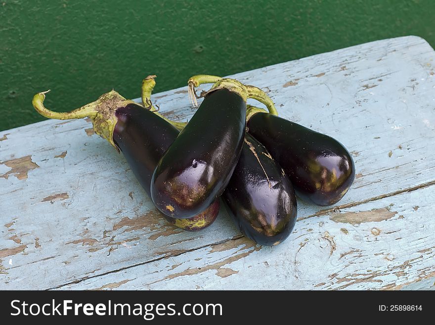 Fresh organic aubergines (eggplants) on blue wooden bench nearby green wall. Fresh organic aubergines (eggplants) on blue wooden bench nearby green wall