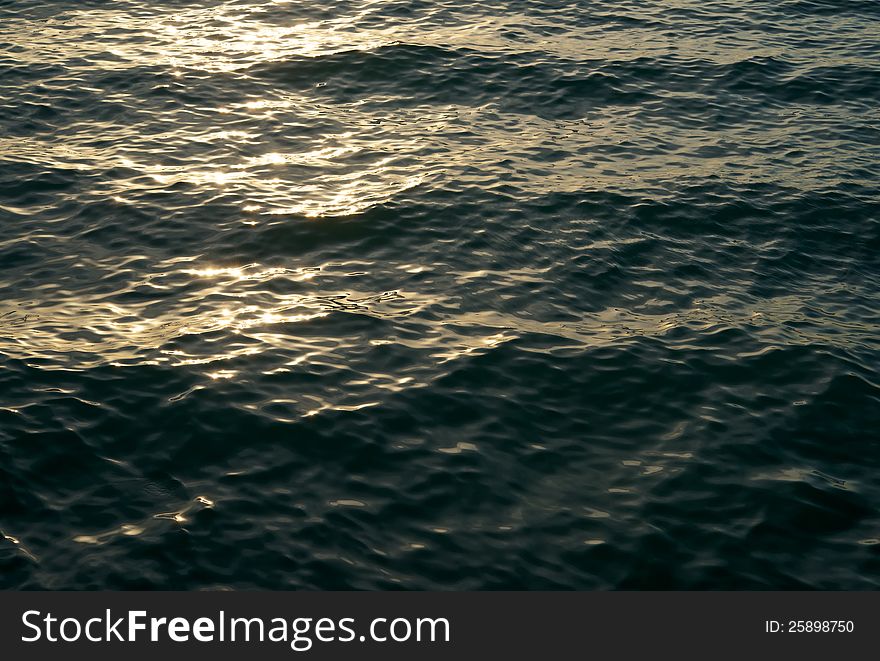 On the surface of the sea play an evening setting sun glare. Shadows on the waves foreshadow the coming night. On the surface of the sea play an evening setting sun glare. Shadows on the waves foreshadow the coming night.