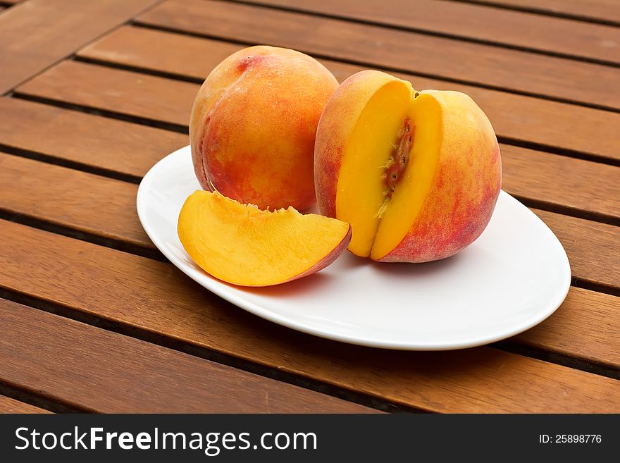 Two fresh peaches on white oval plate on wooden background. Two fresh peaches on white oval plate on wooden background