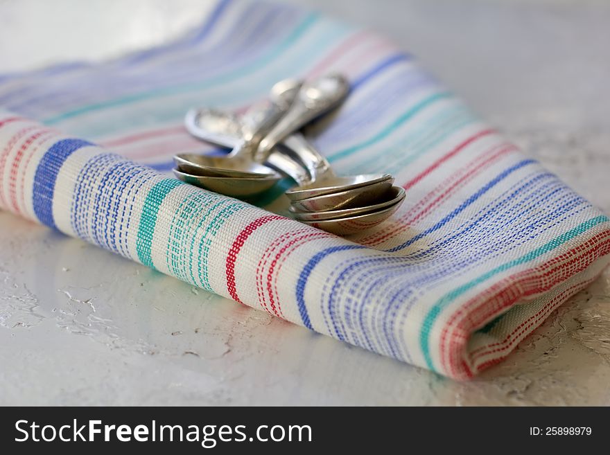 Set of silver teaspoons on the colourful kitchen towel on metallic surface. Set of silver teaspoons on the colourful kitchen towel on metallic surface